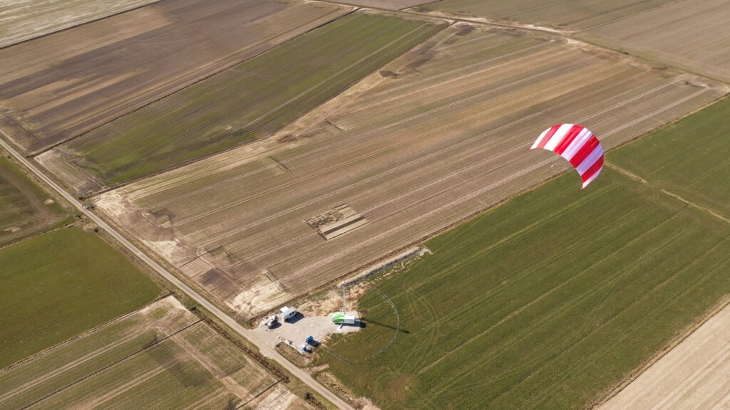 News Blog – a Skysails kite high up in the air above the ground station, surrounded by farmland.