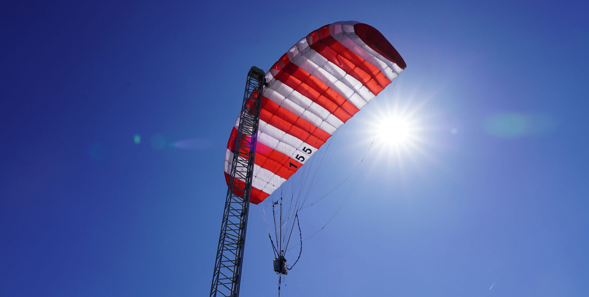 Airborne wind energy system showcasing a kite mounted on a mast, backlit by the sun against a vibrant blue sky.