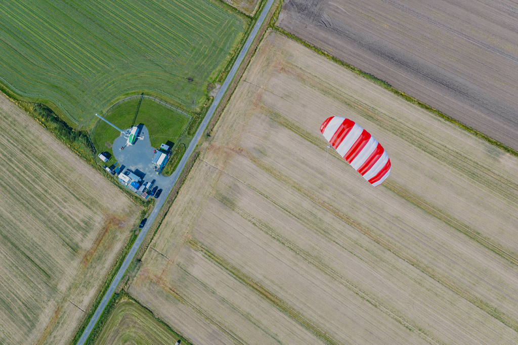 A soft kite soars over the late-summer fields of Klixbüll, Schleswig-Holstein. From above, green pastures blend with brown, harvested fields in a patchwork of color.