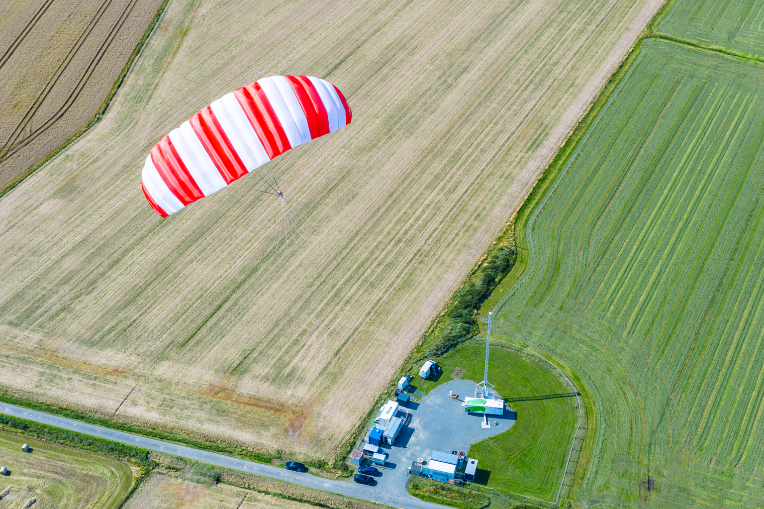 A soft kite soars over the late-summer fields of Klixbüll, Schleswig-Holstein. From above, green pastures blend with brown, harvested fields in a patchwork of color.